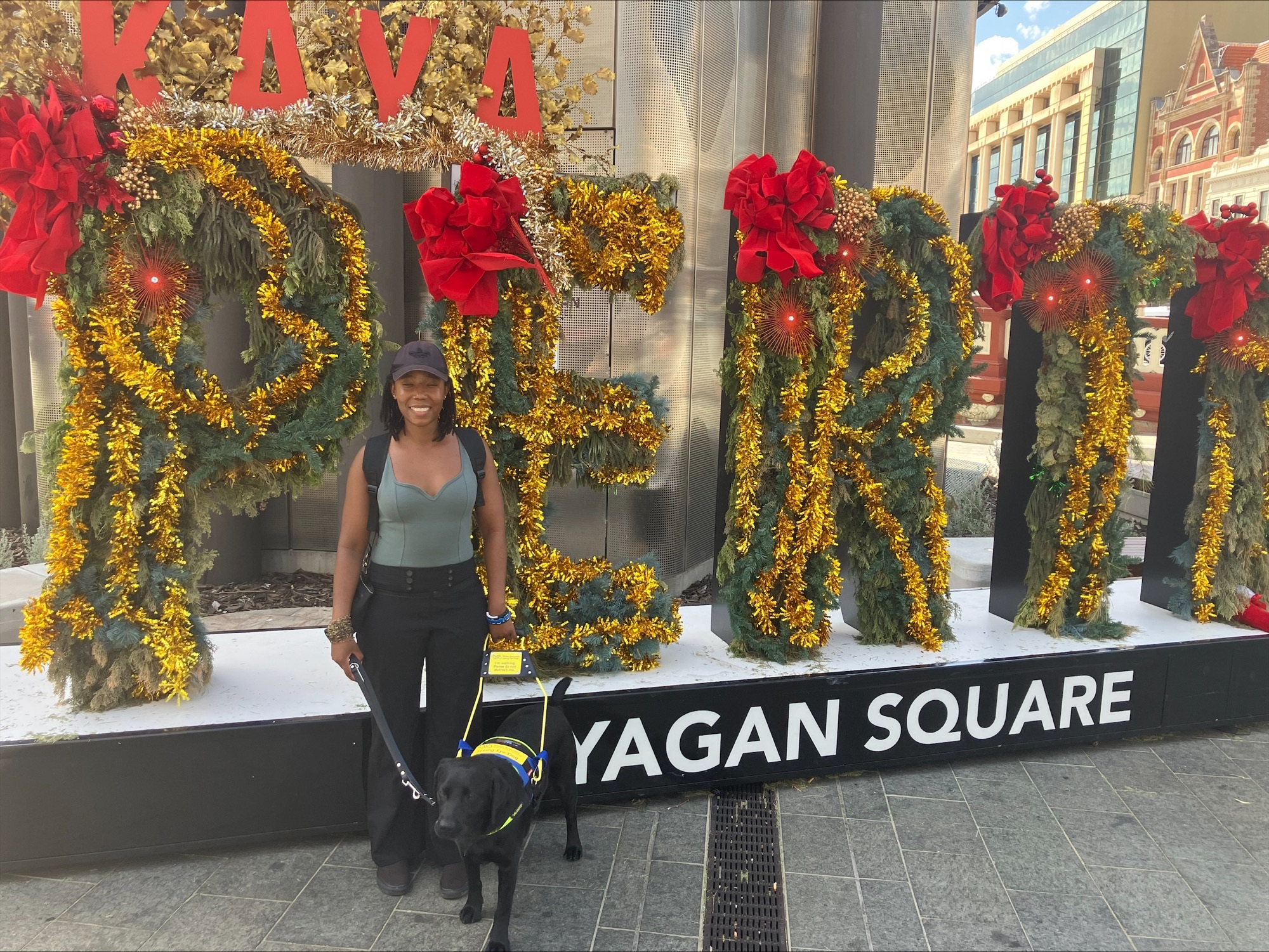 Thayana and seeing eye dog shaylah standing in front of a group of hedge trimmed letters spelling out PERTH